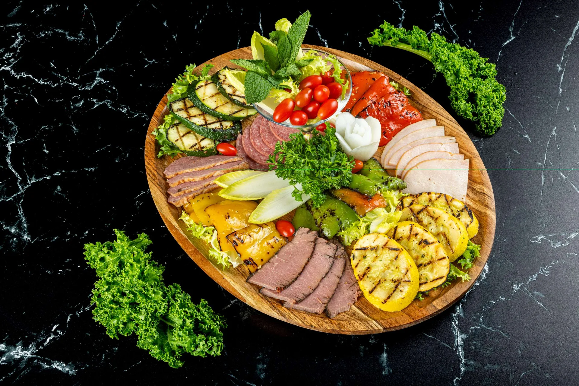 Una tabla de madera con calabacín y calabaza a la parrilla, rosbif, pavo y queso, con una copa de ensalada