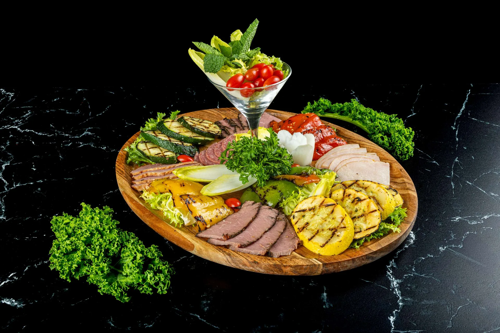 Una tabla de antipasto con verduras a la parrilla, embutidos y queso, con perejil y una copa de ensalada