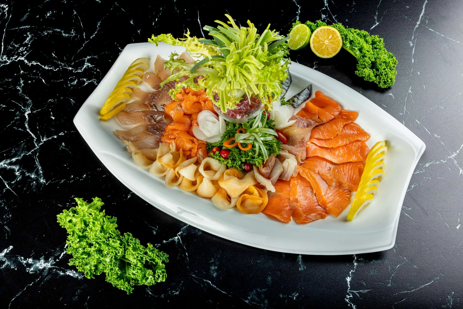 Una fuente blanca de salmón ahumado, pescado blanco y pescado curado con gajos de limón y frisée