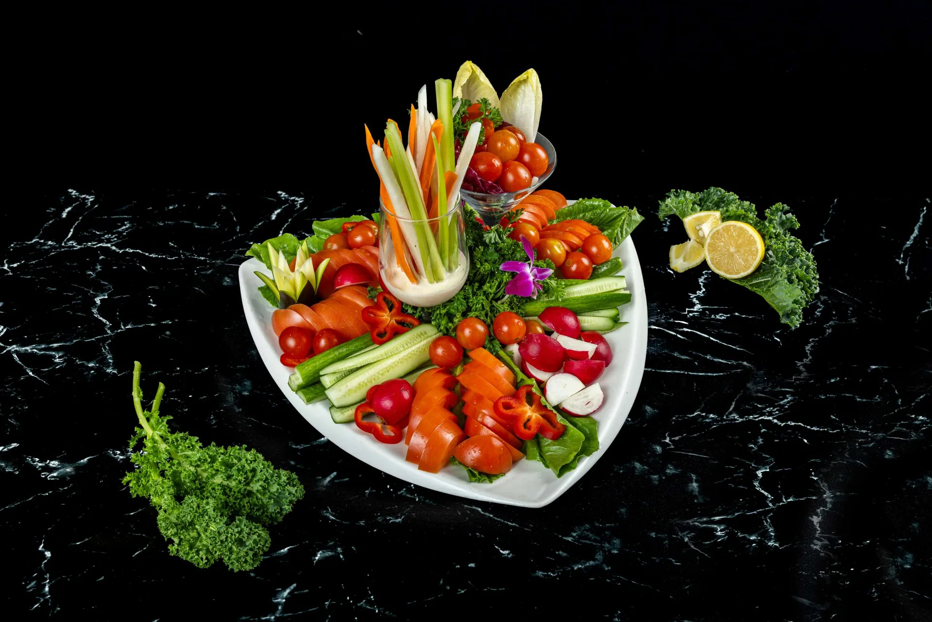 Una fuente de tomates cherry, rábanos, bastones de verdura y mozzarella alrededor de una copa de crudités