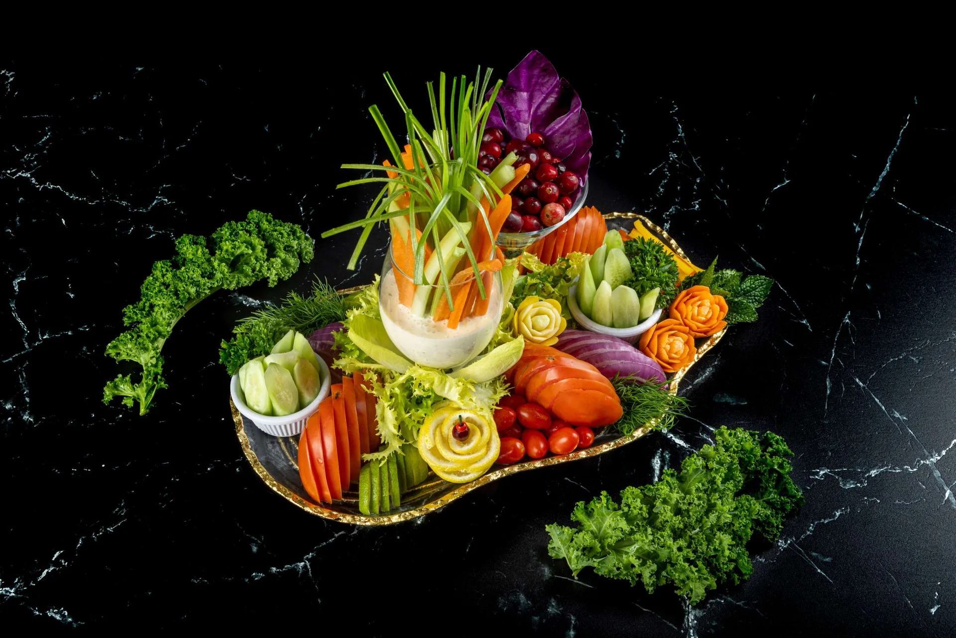 Un arreglo de crudités con cebollino y endivia en una bandeja de borde dorado, rodeado de perejil rizado