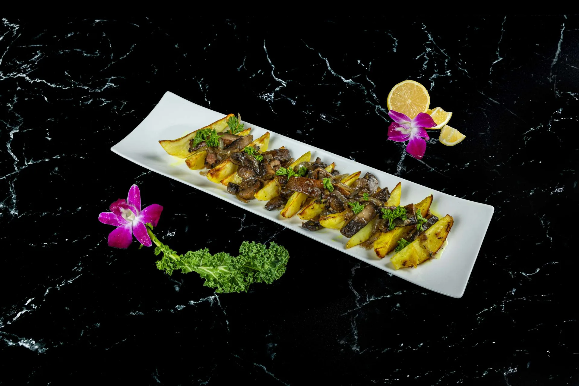 Gajos de patata asada y champiñones alineados en una fuente rectangular larga con limón