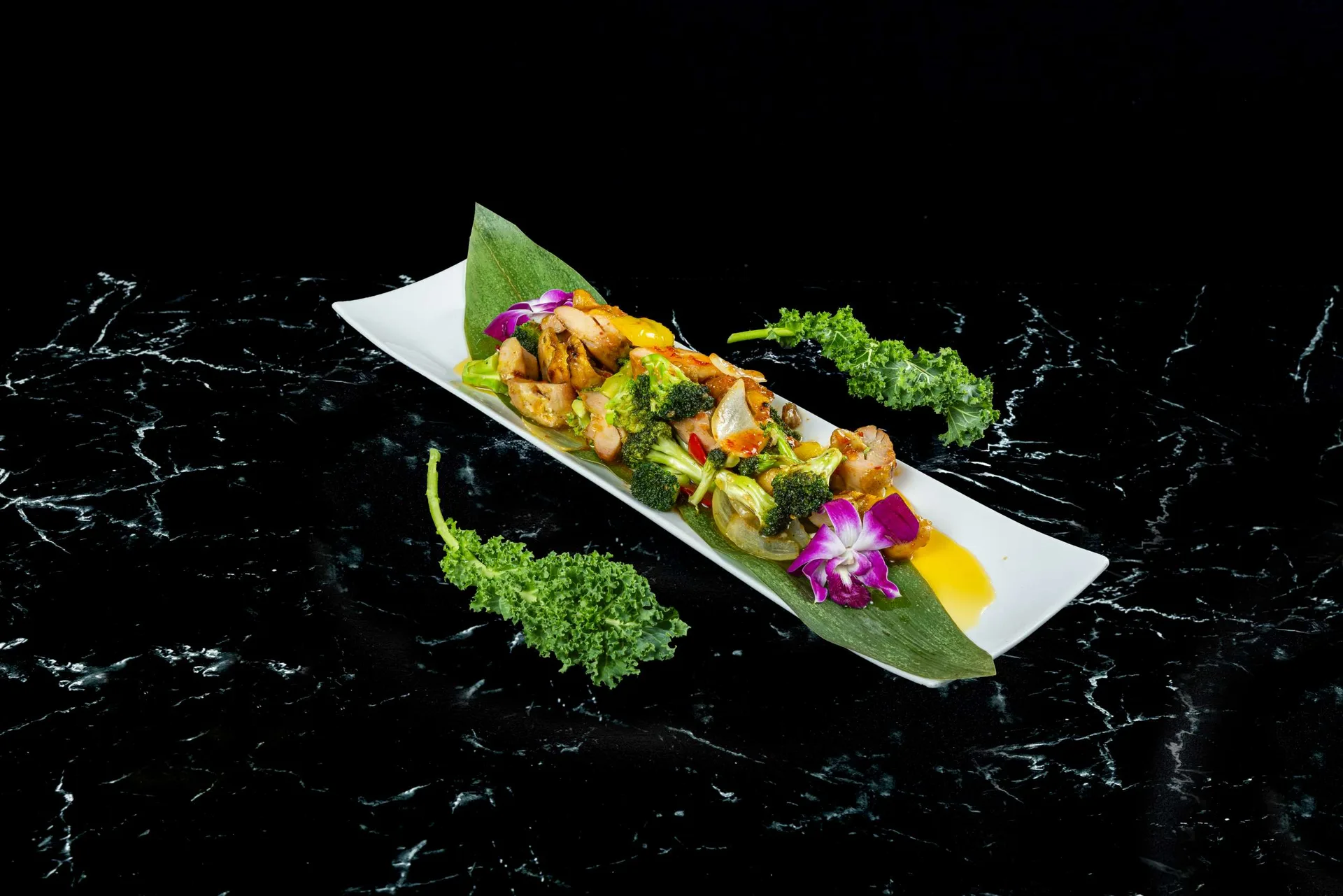 Gambas y verduras servidas sobre una hoja de plátano en una fuente blanca larga con mango