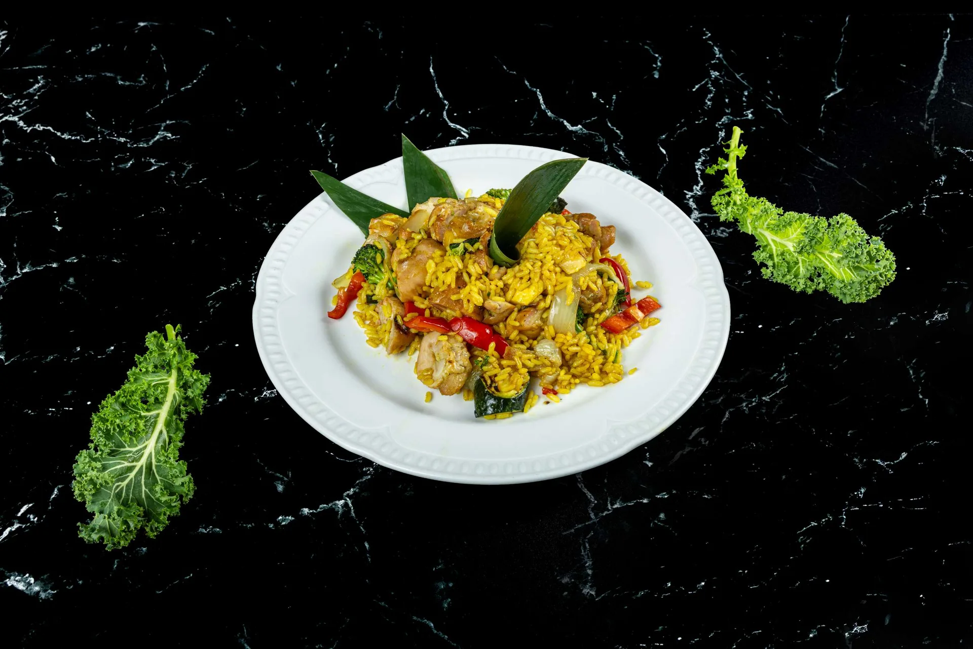 Pollo y verduras sobre arroz amarillo al azafrán en un plato blanco redondo con laurel