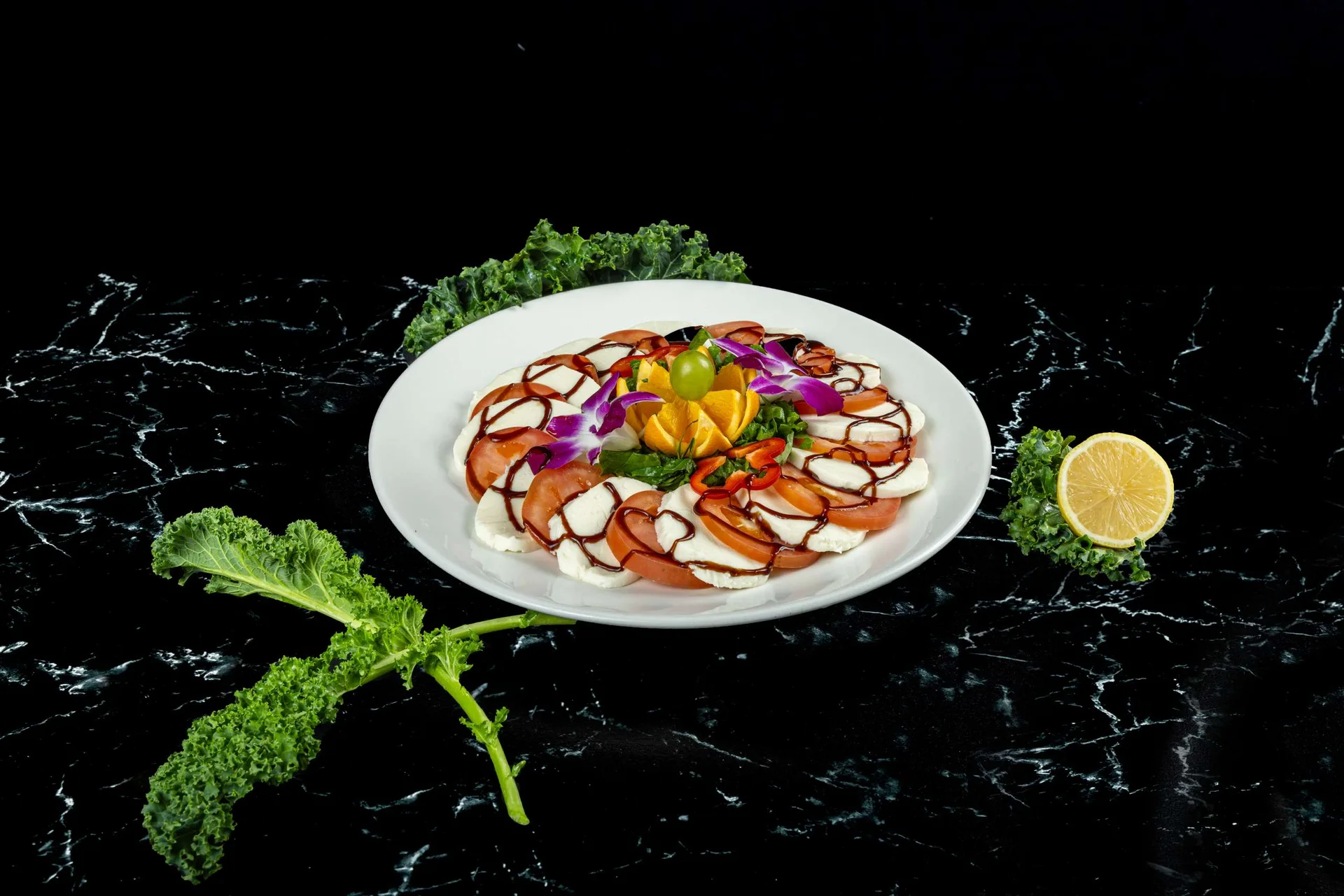 Un plato redondo de rodajas de mozzarella y tomate en círculo con albahaca y balsámico