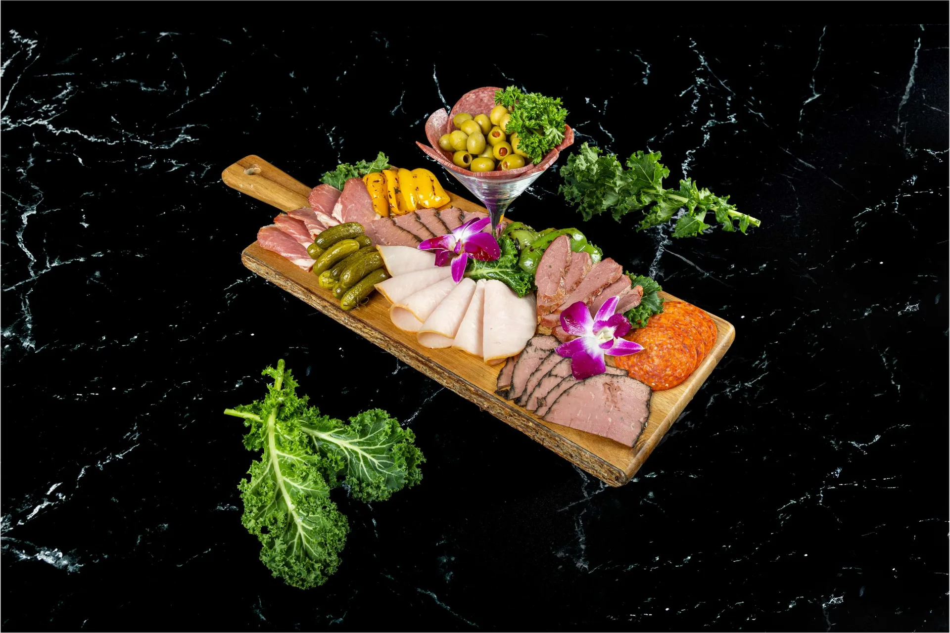 Una tabla de madera con pavo, rosbif y salami en lonchas y una copa de ensalada de maíz