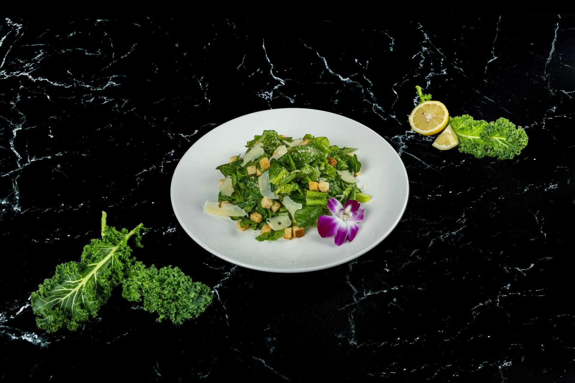 Una ensalada picada de maíz, pepino y picatostes en un plato blanco redondo con limón y una orquídea