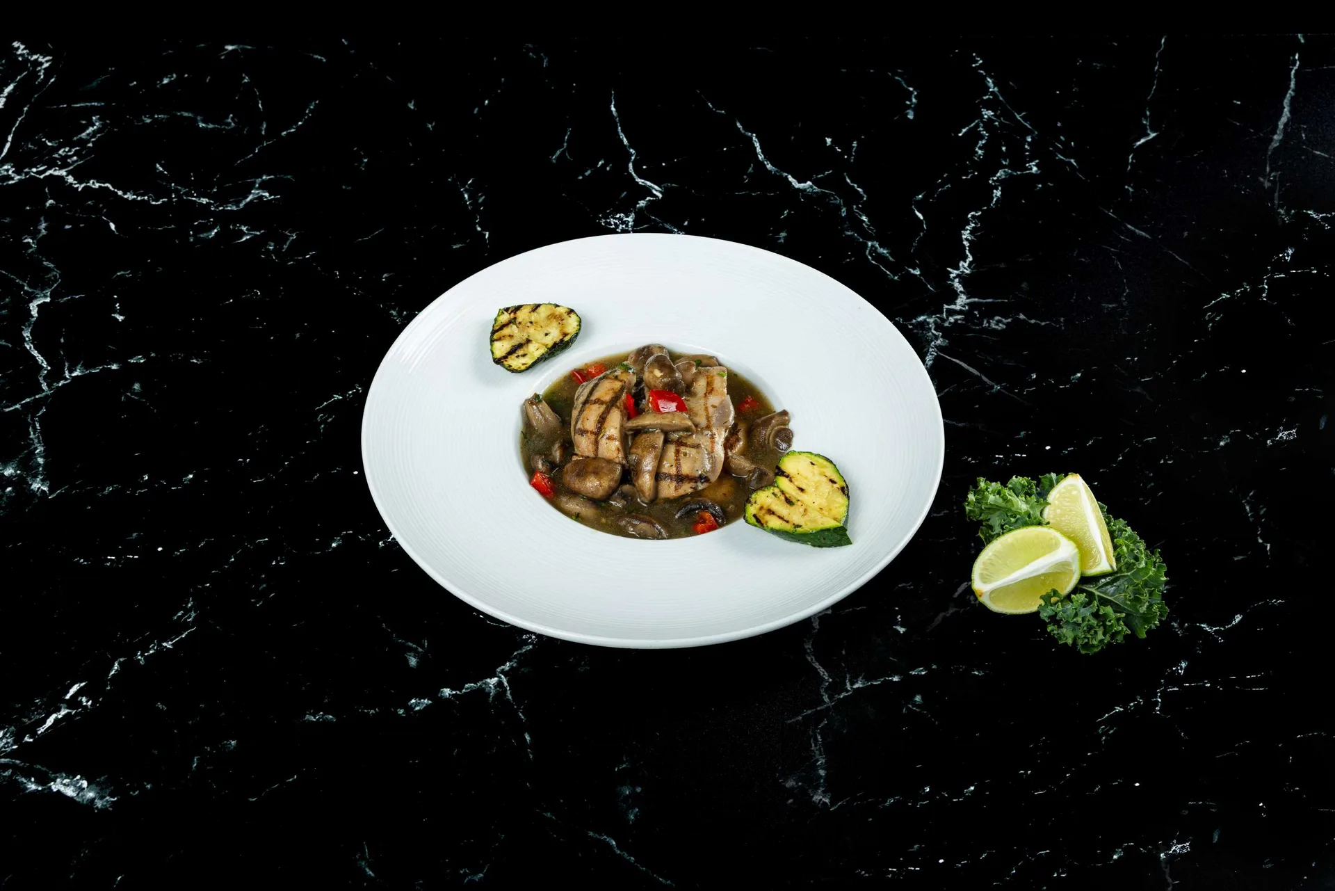 Pollo a la parrilla con champiñones, calabacín y pimientos en un plato blanco redondo con lima