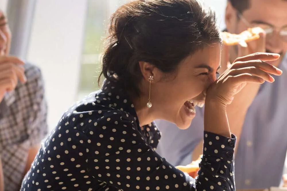 Laughing businesswoman at corporate luncheon eating pizza and enjoying lunch together with colleagues