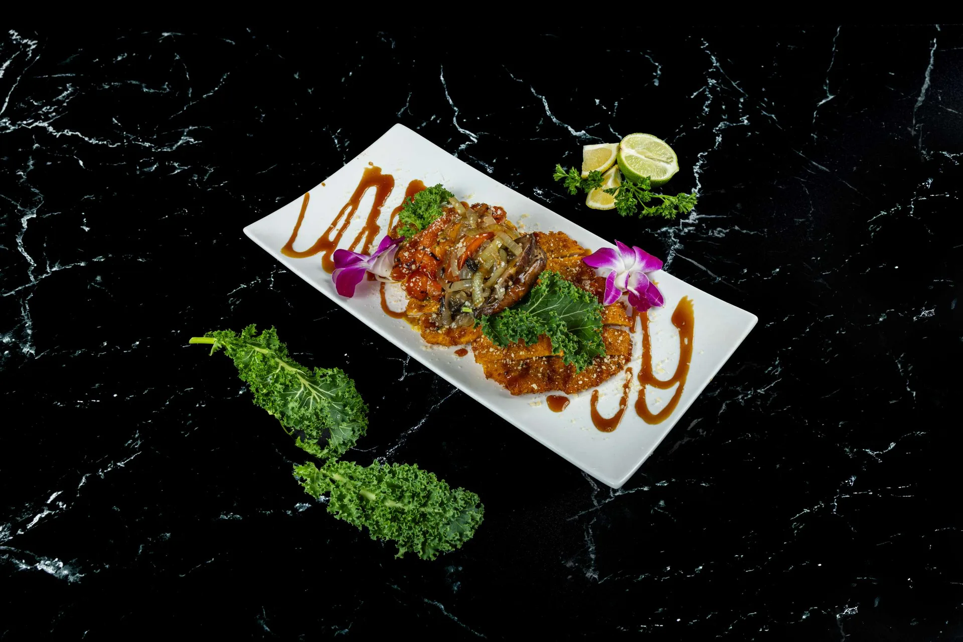 Escalopes empanados en una fuente rectangular con un trazo de salsa oscura y una orquídea