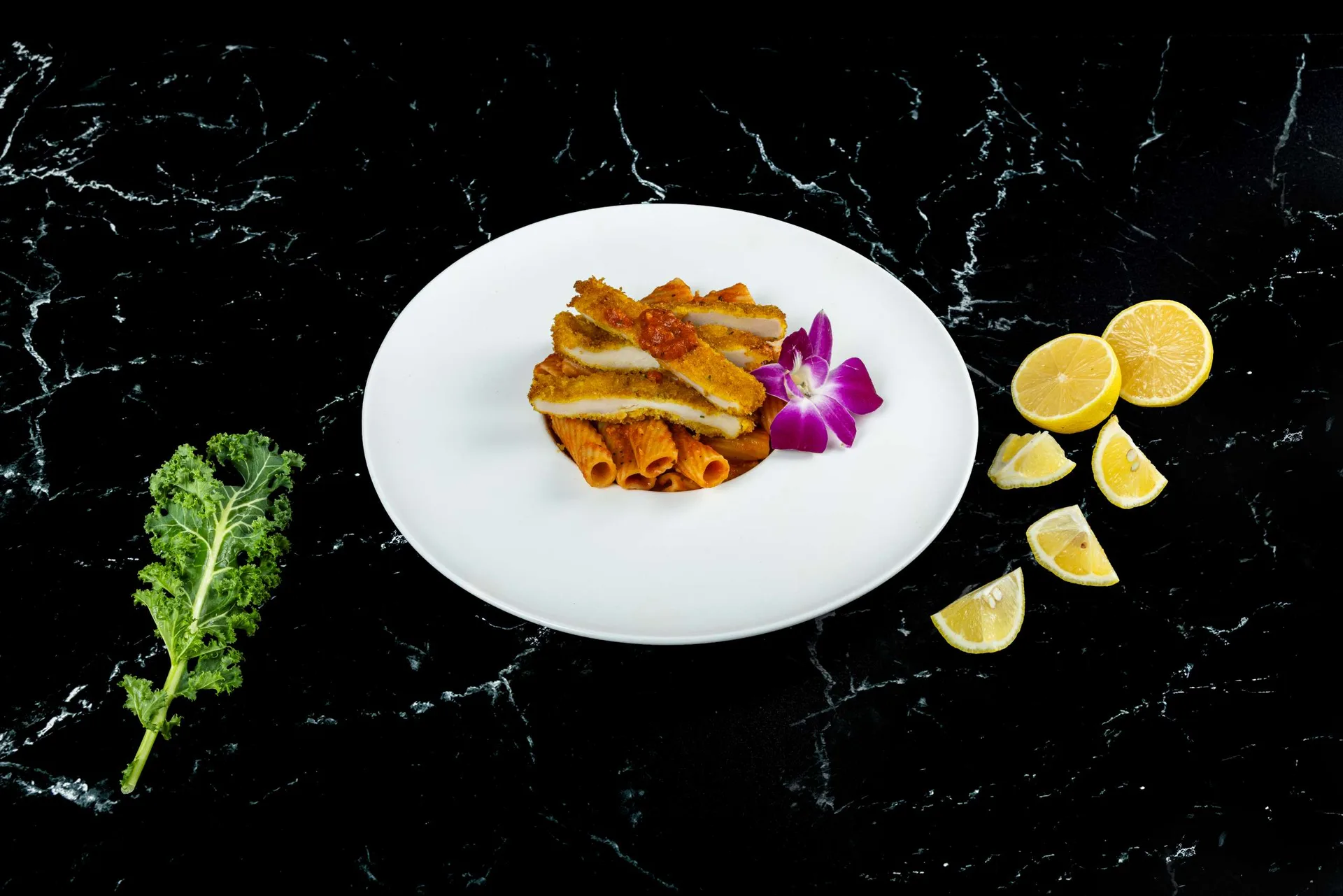 Penne en salsa de tomate en un plato blanco redondo con una orquídea y gajos de limón