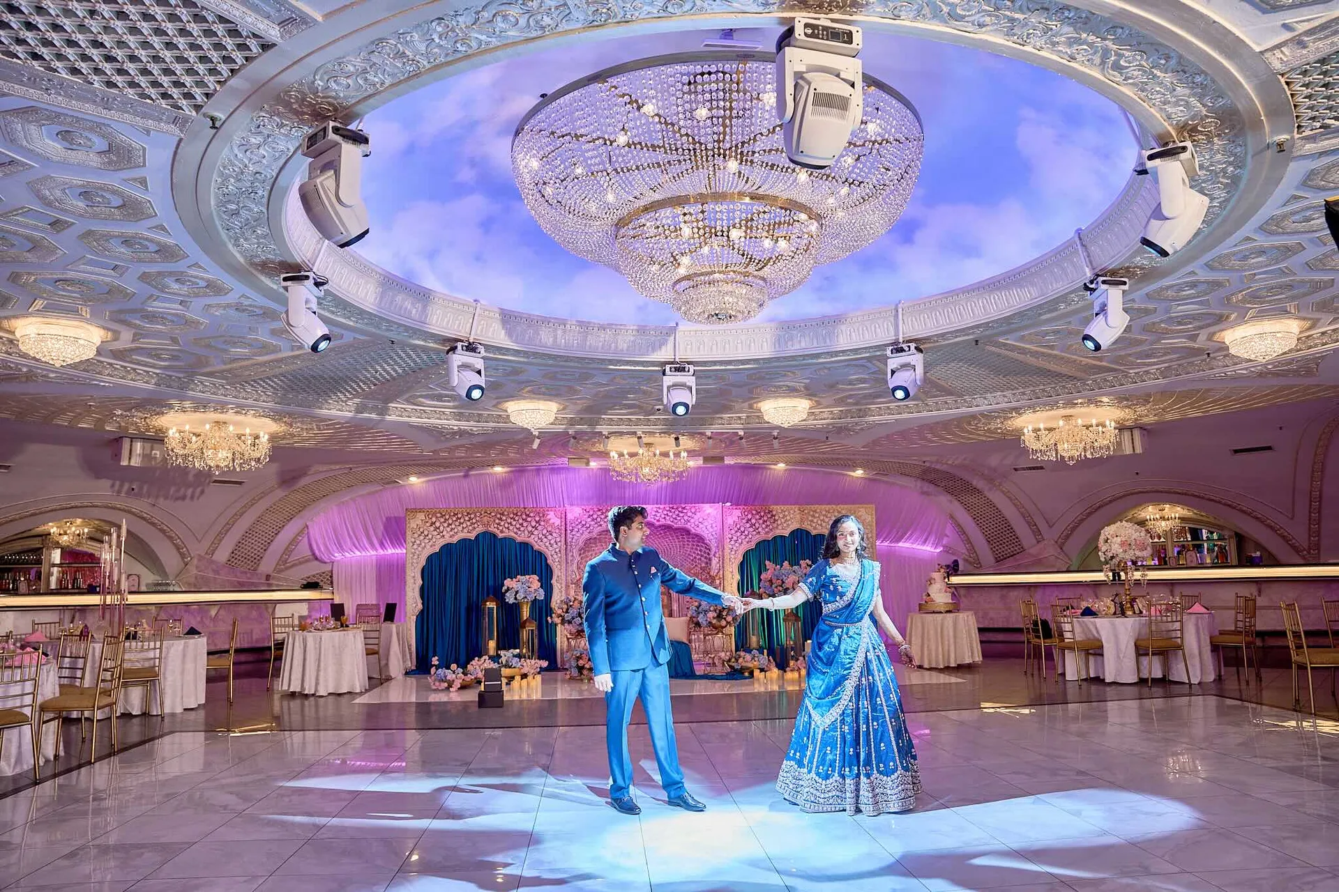 Una pareja baila sobre la pista iluminada bajo la cúpula, ella con un sari azul y él con traje azul