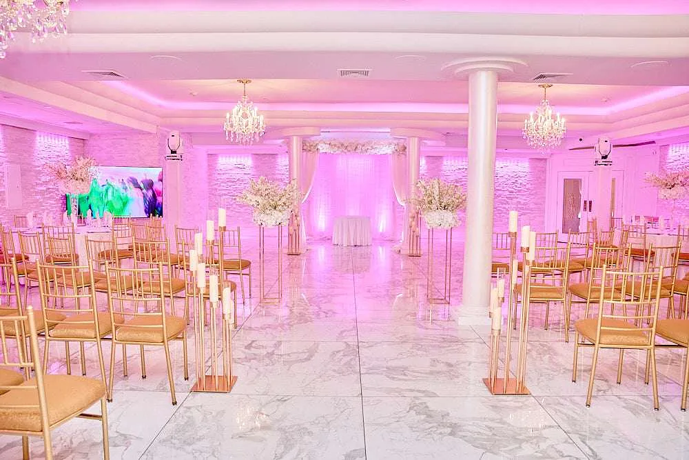 Gold pedestals of white flowers lining the marble floor between columns, the room washed in pink
