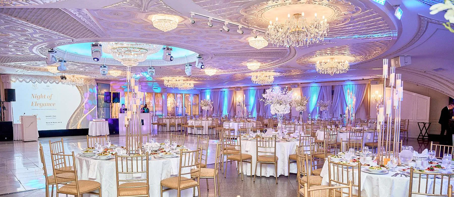 El salón de Floral Terrace con luz lavanda, mesas redondas, sillas doradas y altos centros de flores blancas