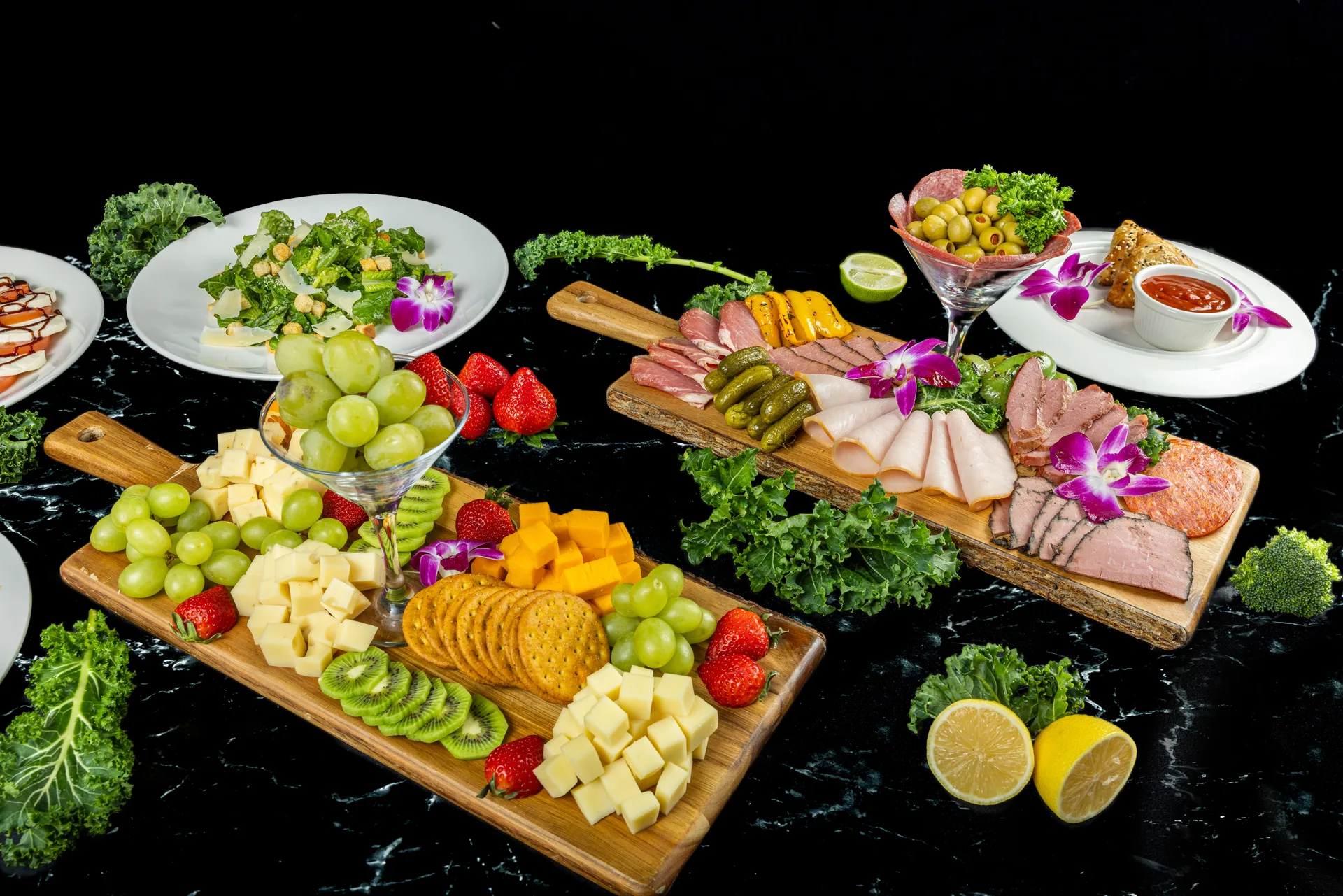 Dos tablas largas de madera con queso, galletas, uvas, kiwi y fresas junto a embutidos