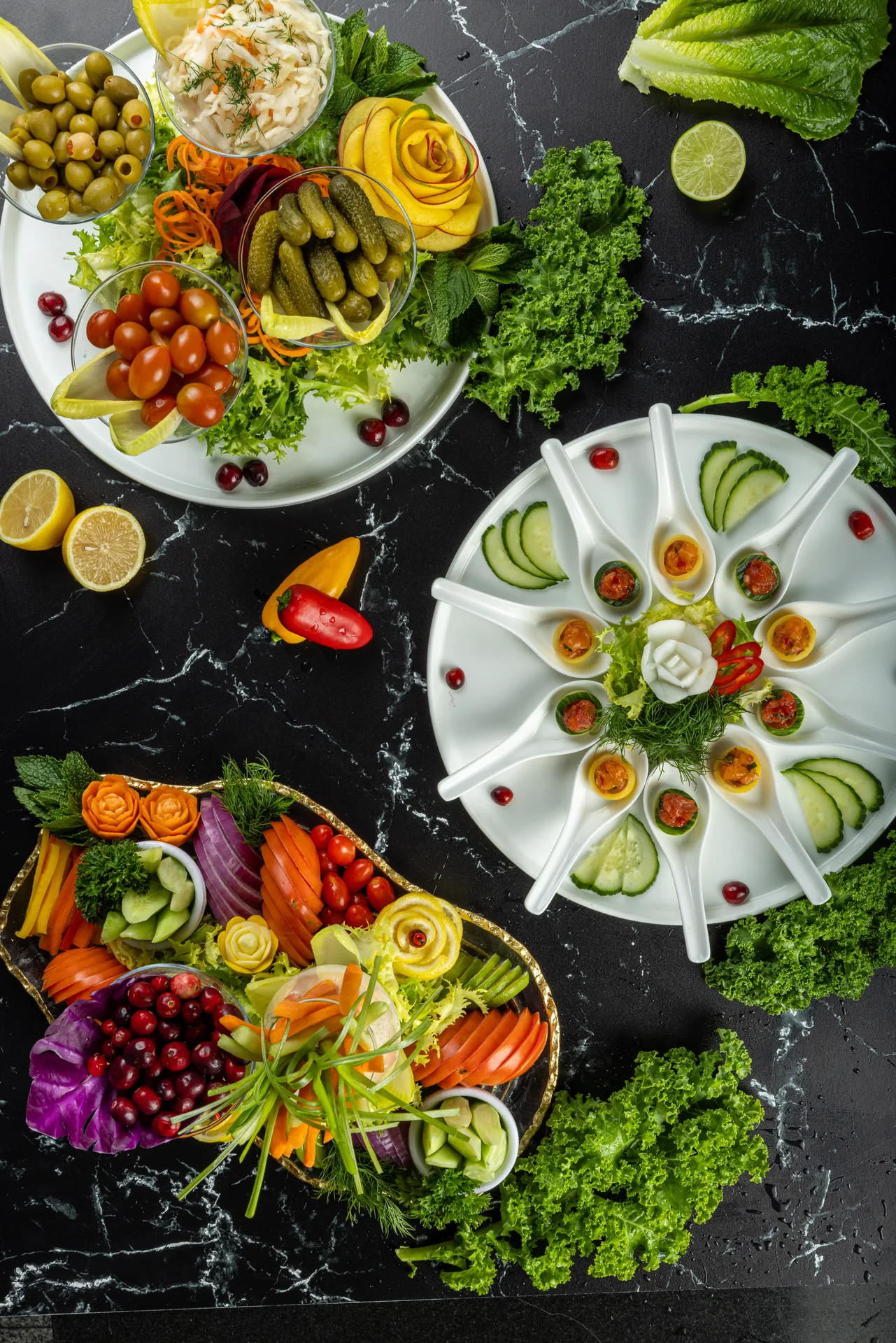 Una estación de ensaladas con aceitunas, pepinillos y rosas de zanahoria junto a una fuente de amuse-bouche