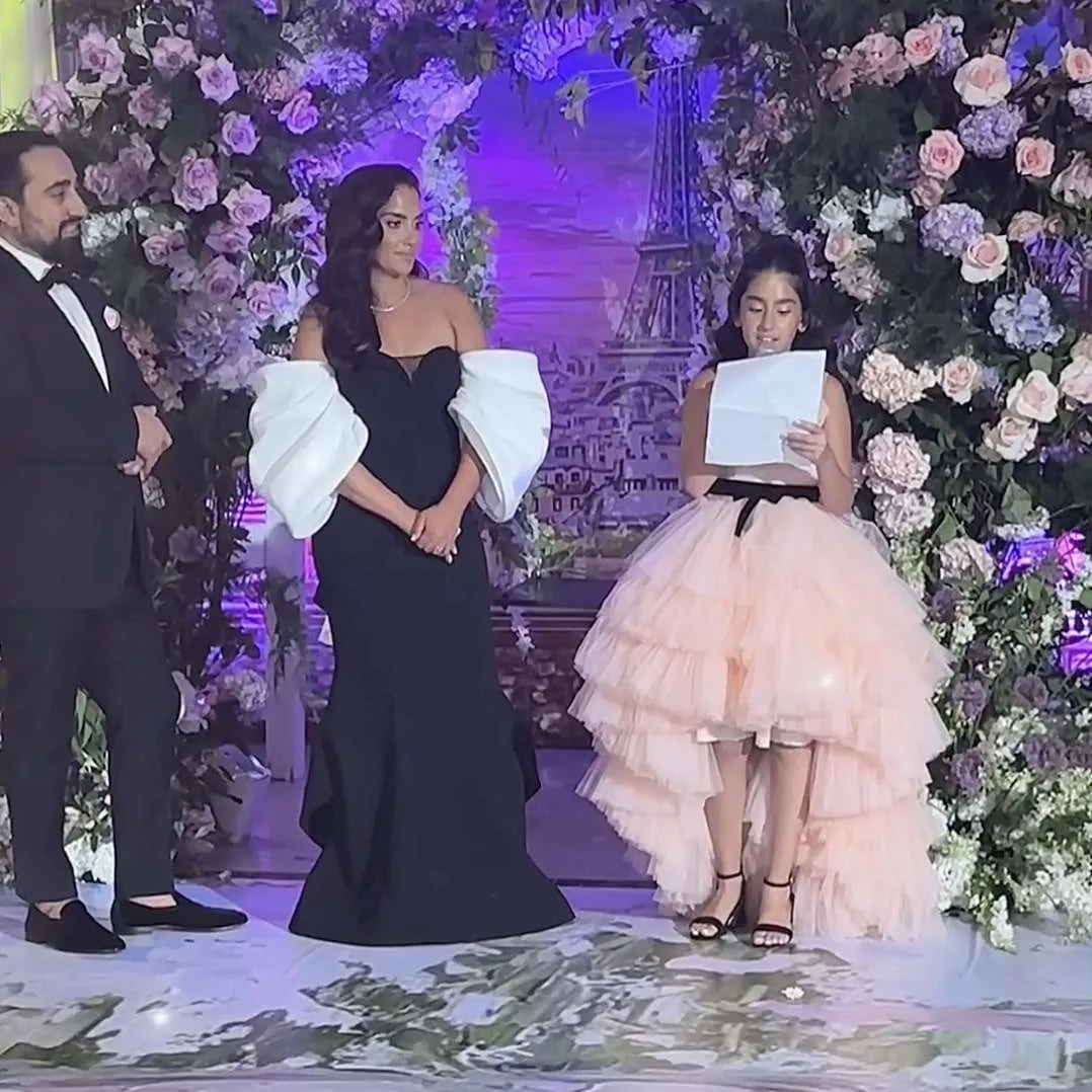 La joven homenajeada lee un discurso junto a sus padres ante un arco de rosas y hortensias