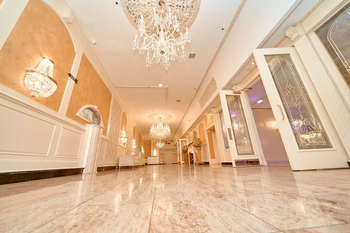 Una galería larga de paredes albaricoque con arañas de cristal sobre boiserie blanca y mármol pulido