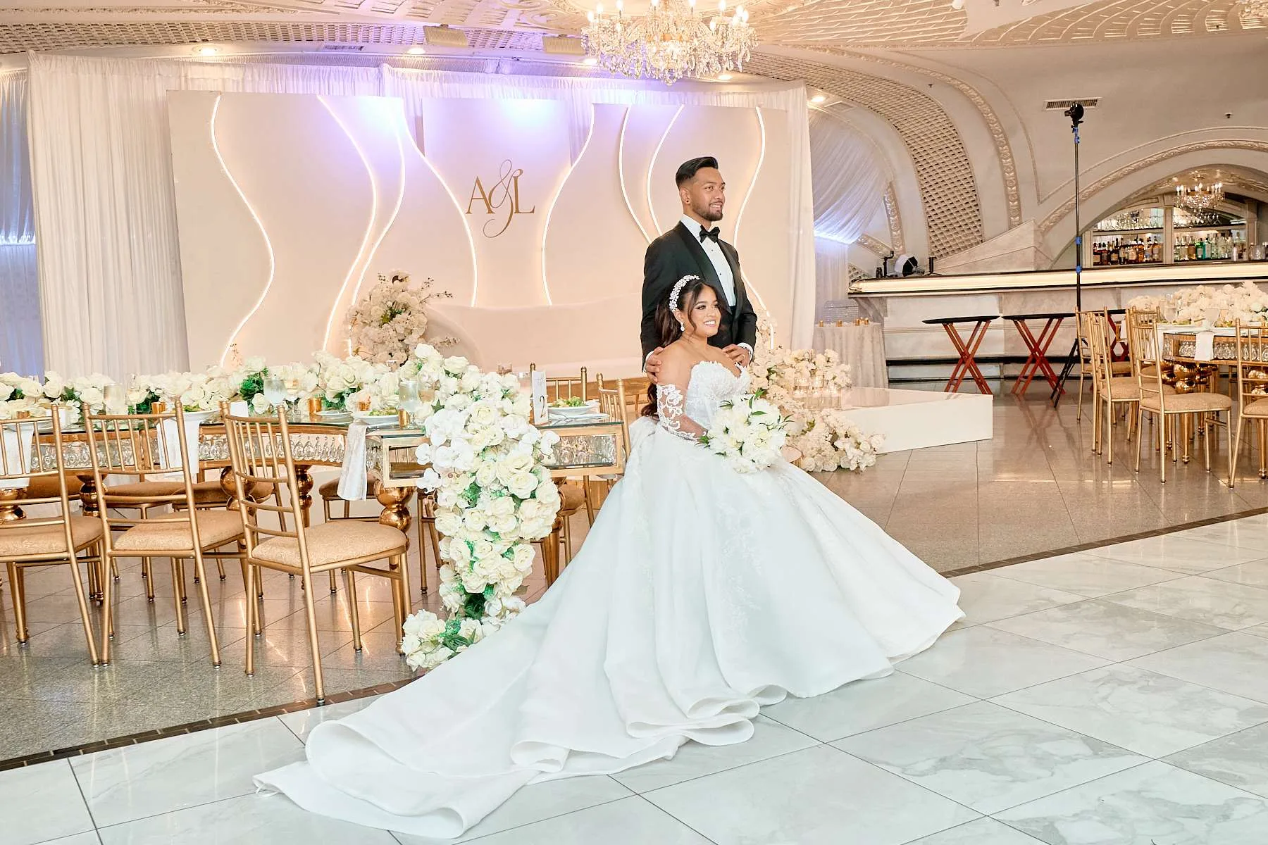 Una pareja ante un fondo de cortinaje blanco con su monograma, enmarcado por arreglos florales blancos