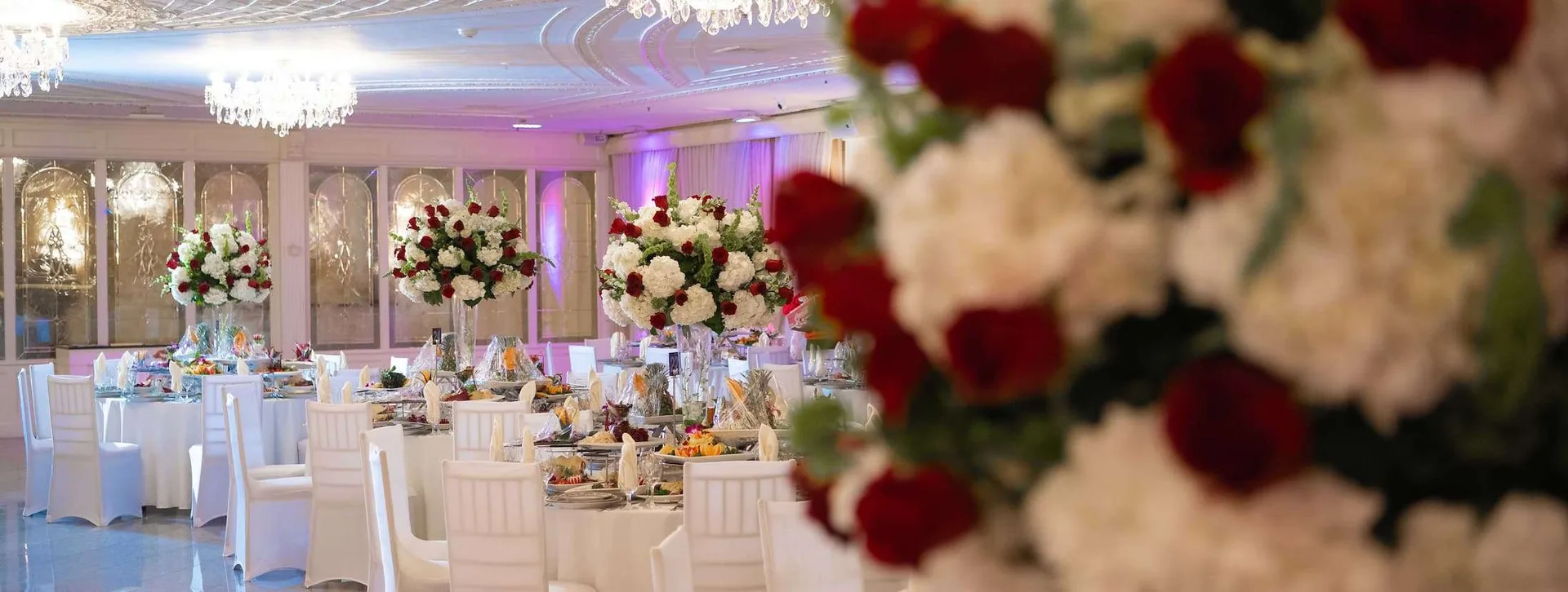 Rosas blancas y burdeos en primer plano de un salón vestido de blanco, con arañas al fondo