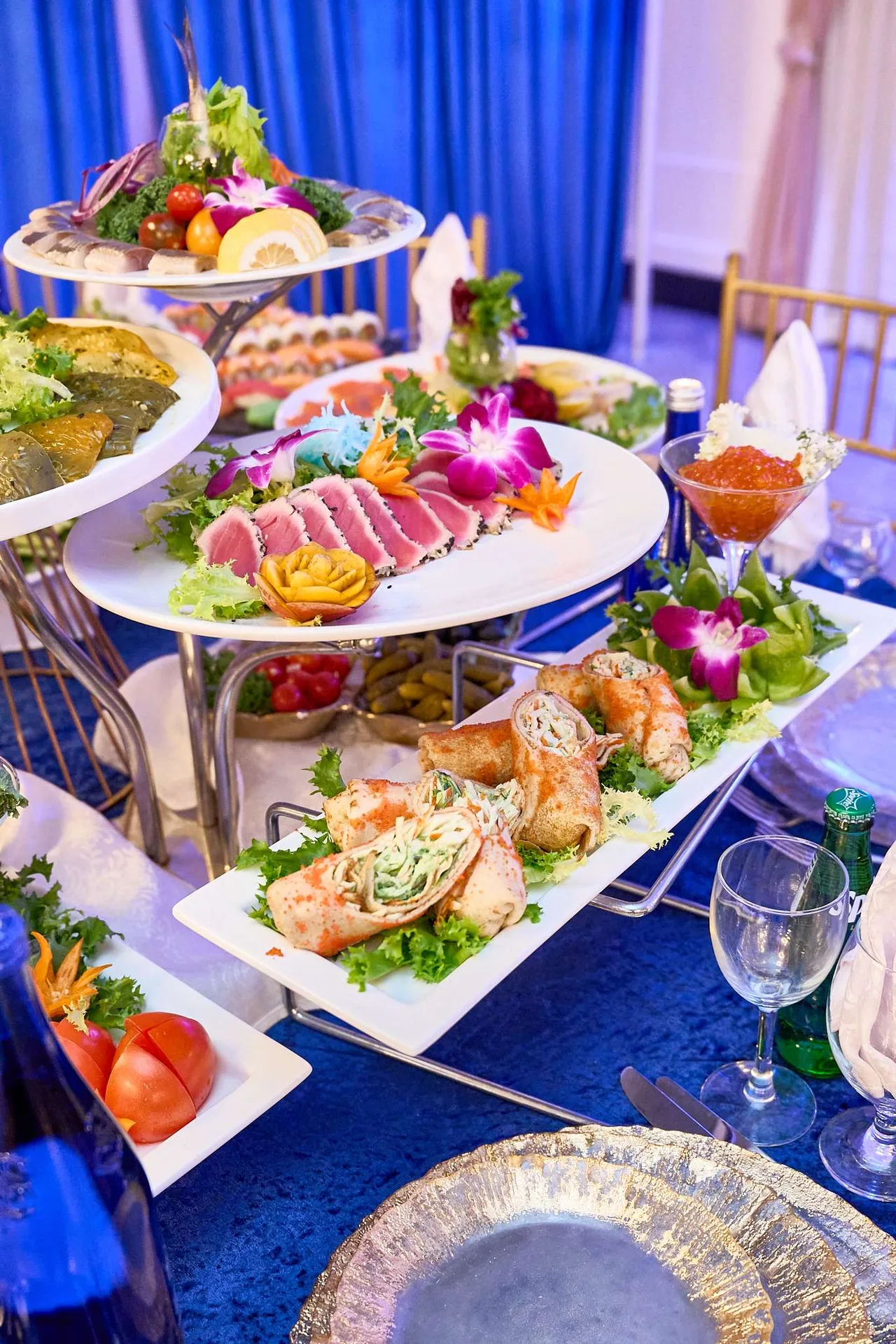 Bandejas escalonadas de sashimi, rollos de sushi, langostinos y fruta sobre un mantel azul