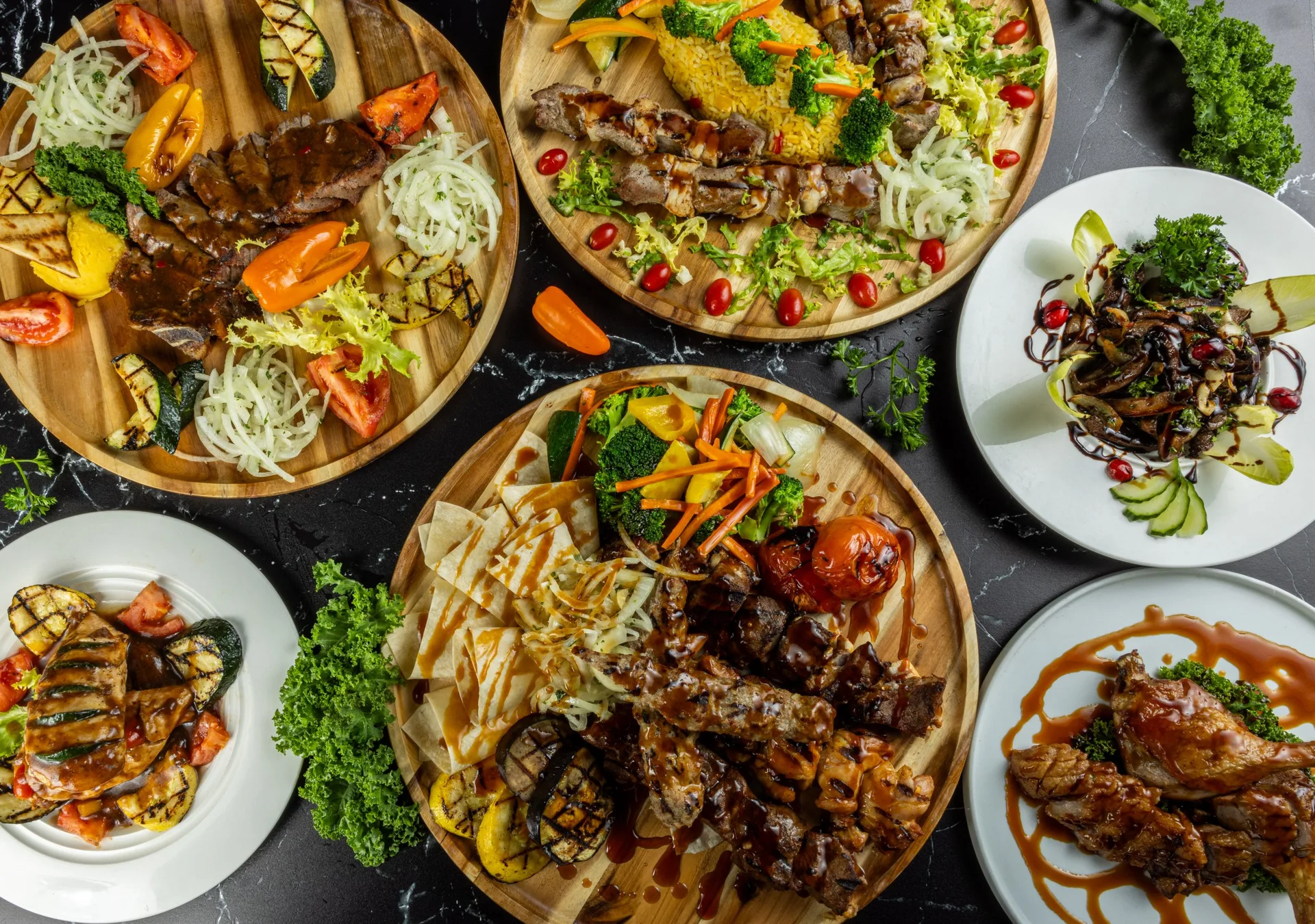 Tablas de madera con brochetas a la parrilla, pan plano, pimientos y ensaladas de hierbas, vistas desde arriba sobre mármol negro
