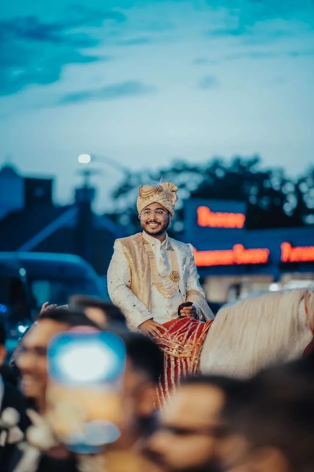 El baraat llega al anochecer, el novio a caballo con el letrero iluminado de Floral Terrace detrás