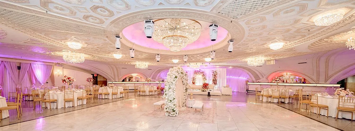 El salón con un arco de mandap de flores blancas en el centro y sillas doradas a ambos lados
