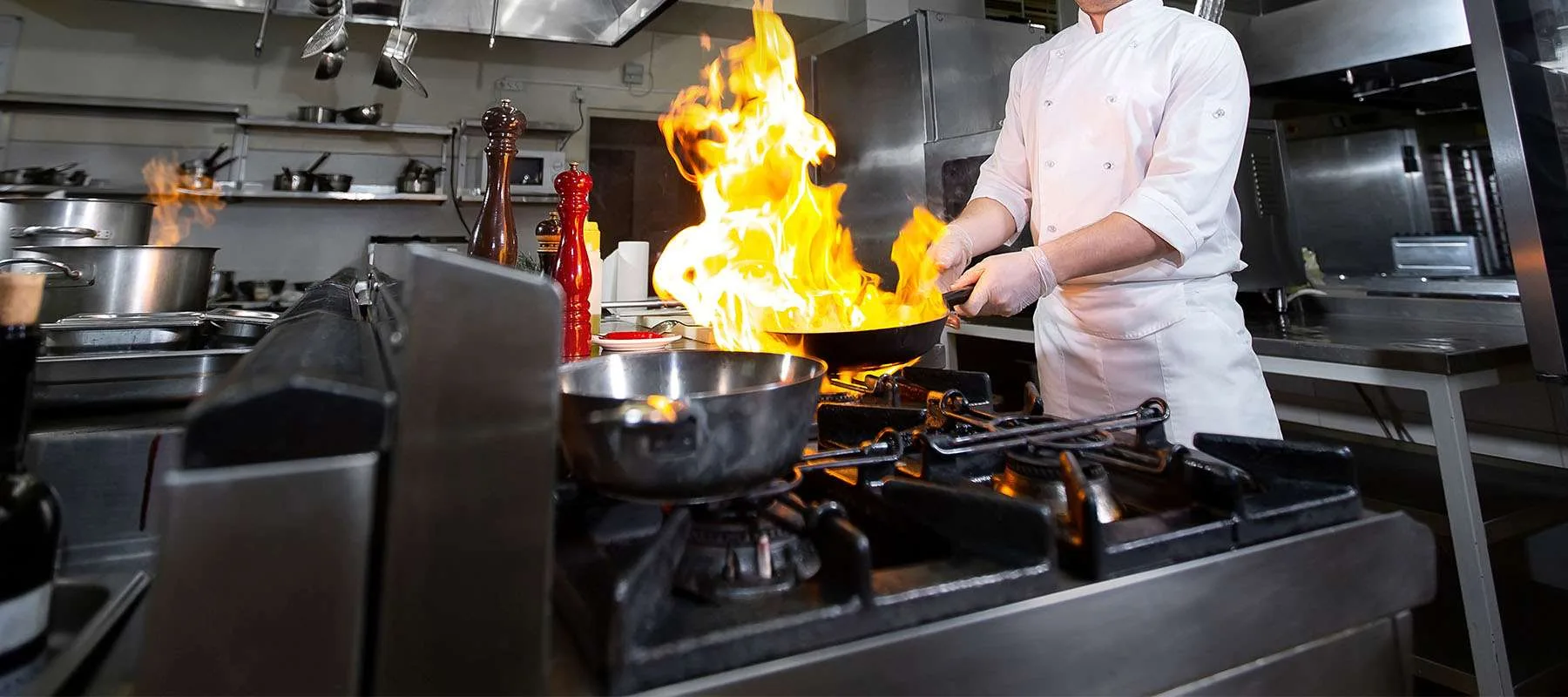 Un cocinero de blanco inclina una sartén sobre la llama abierta de los fogones