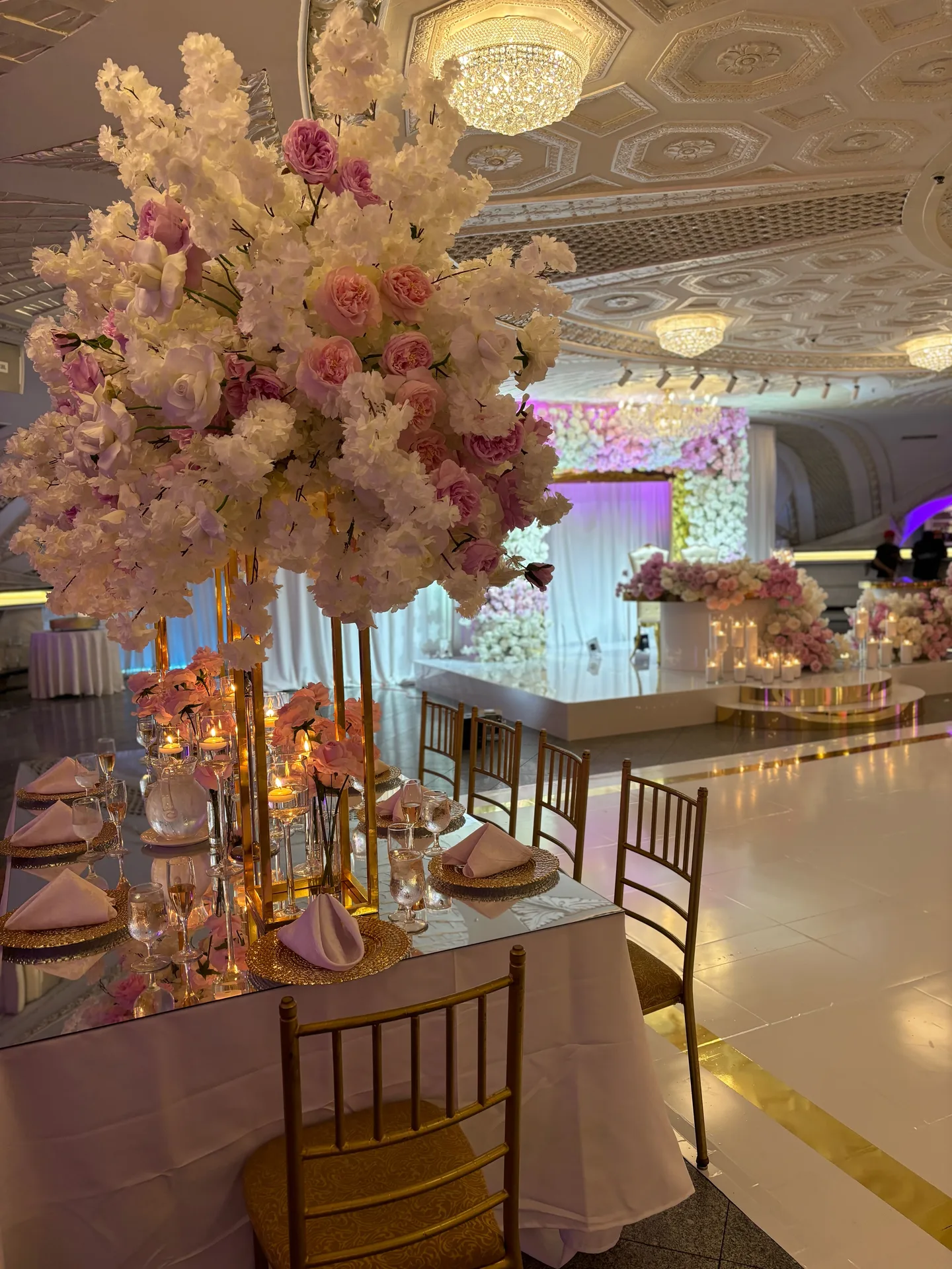 La mesa presidencial con un árbol de flores rosadas y sillas doradas, con la pista blanca y un fondo floral al fondo