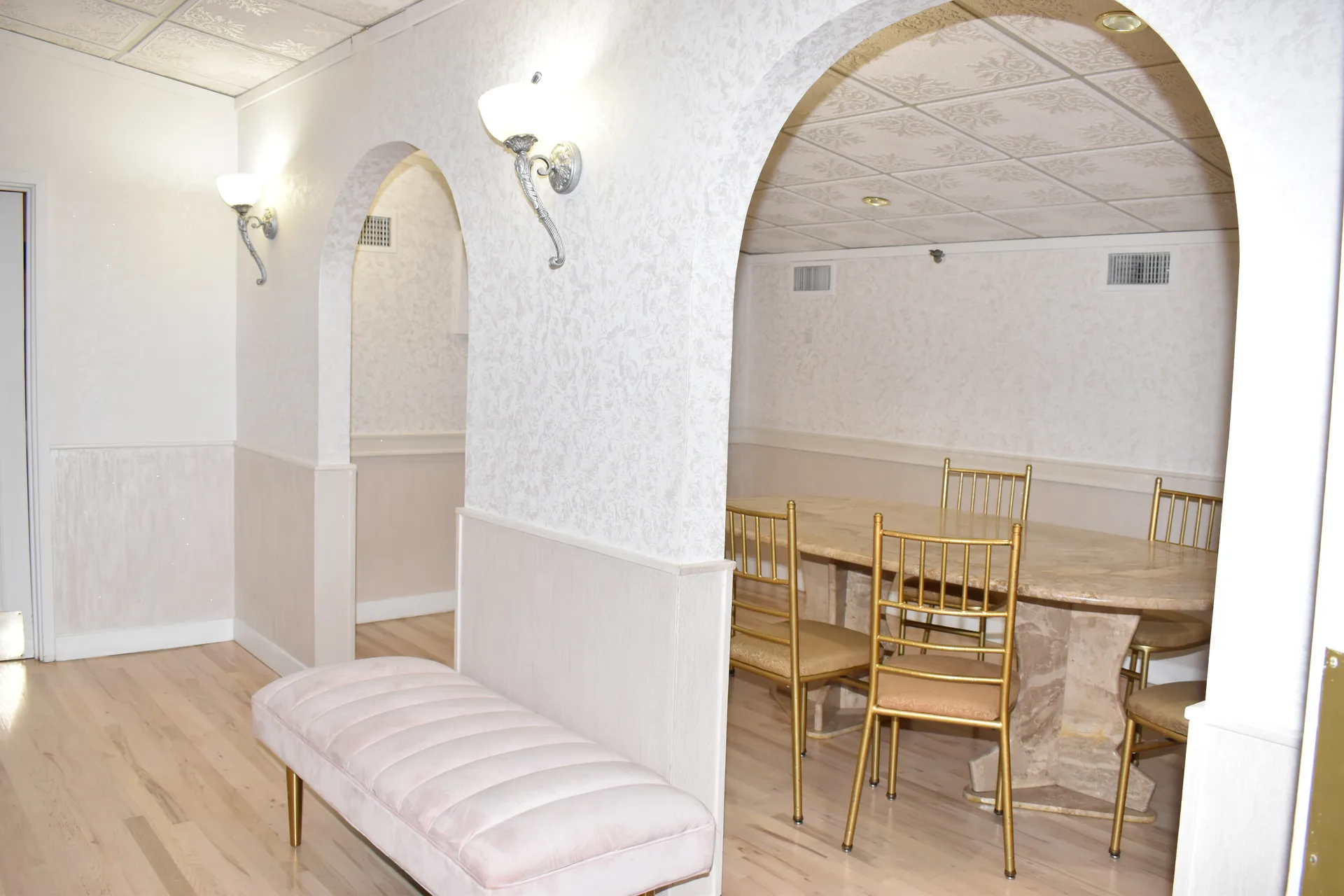 Una alcoba con arco en la suite con una mesa de comedor de piedra y sillas doradas, y enfrente un banco tapizado en rosa